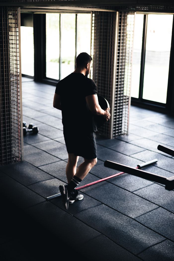 services-01 Athletic man working out in a modern gym, holding weights near large windows.