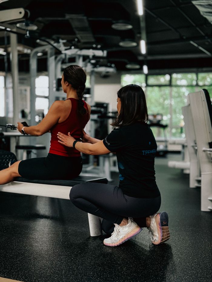 heros-img A personal trainer helps a woman with her exercise routine in a modern gym environment.