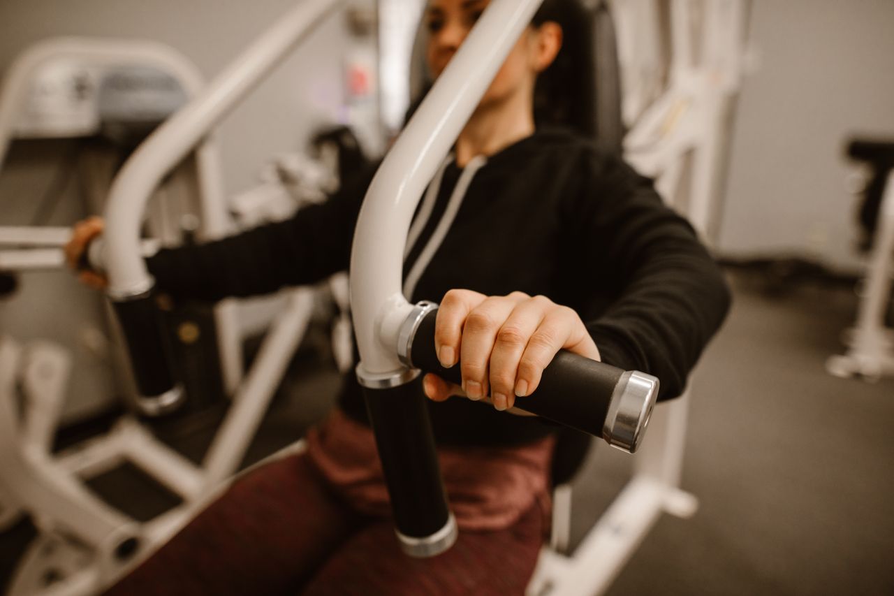 about-us Close-up of a woman using a chest press machine in the gym for strength training.