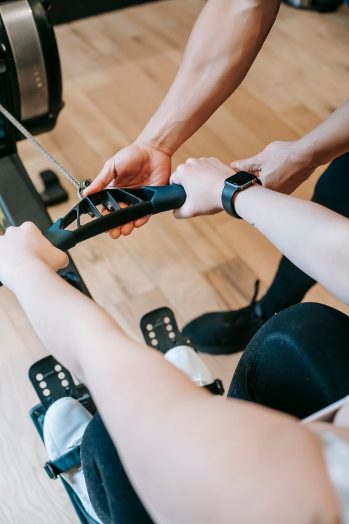services-02 High angle of crop anonymous trainer assisting woman exercising on rowing machine in sports club