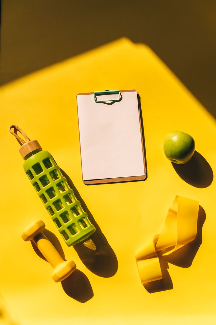 our-story Bright flat lay of fitness essentials including dumbbells, water bottle, and apple on a yellow background.