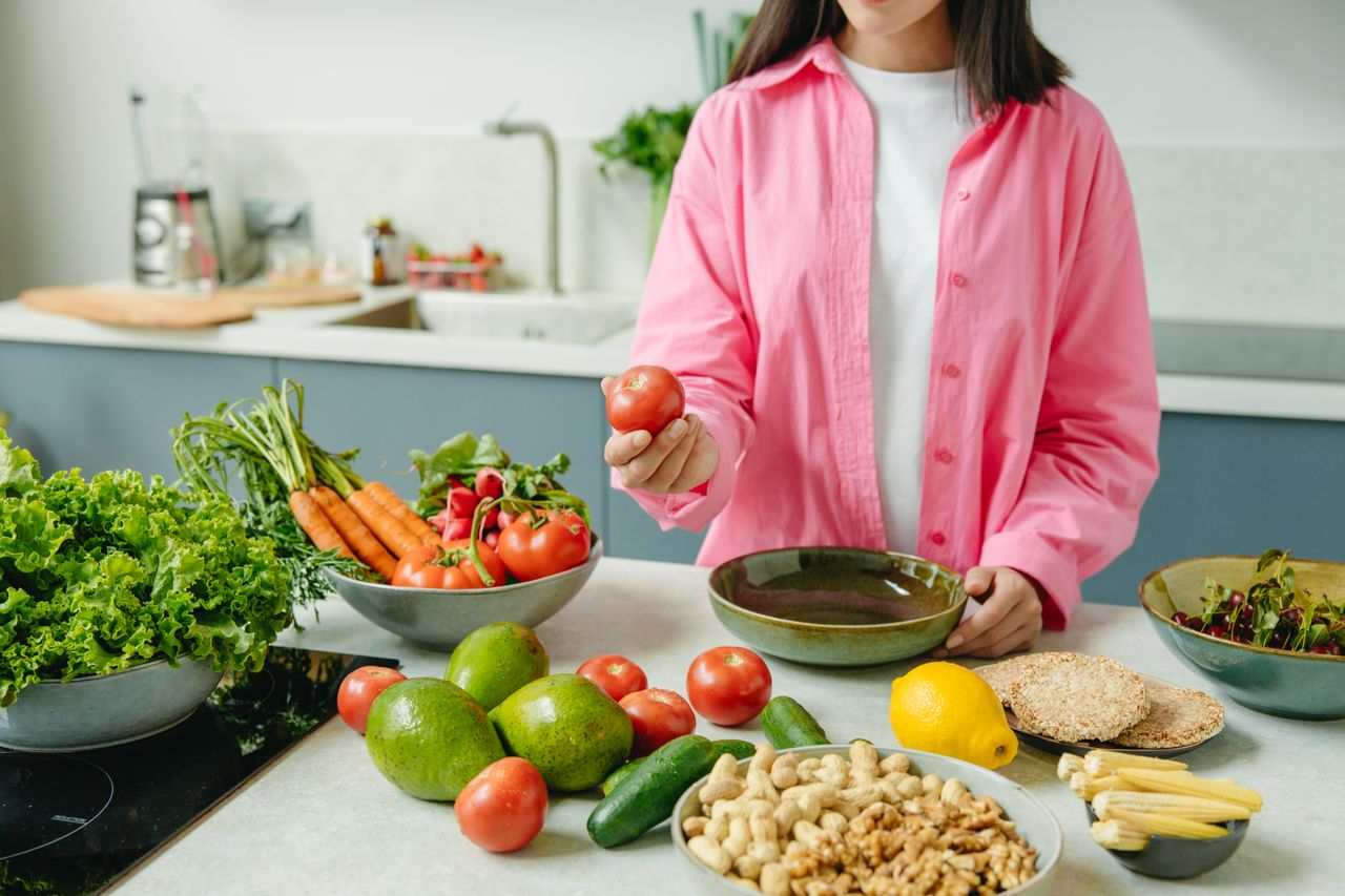 Crafting Captivating Headlines: Your awesome post title goes here Woman in pink overshirt holds tomato in kitchen with fresh fruits and veggies.